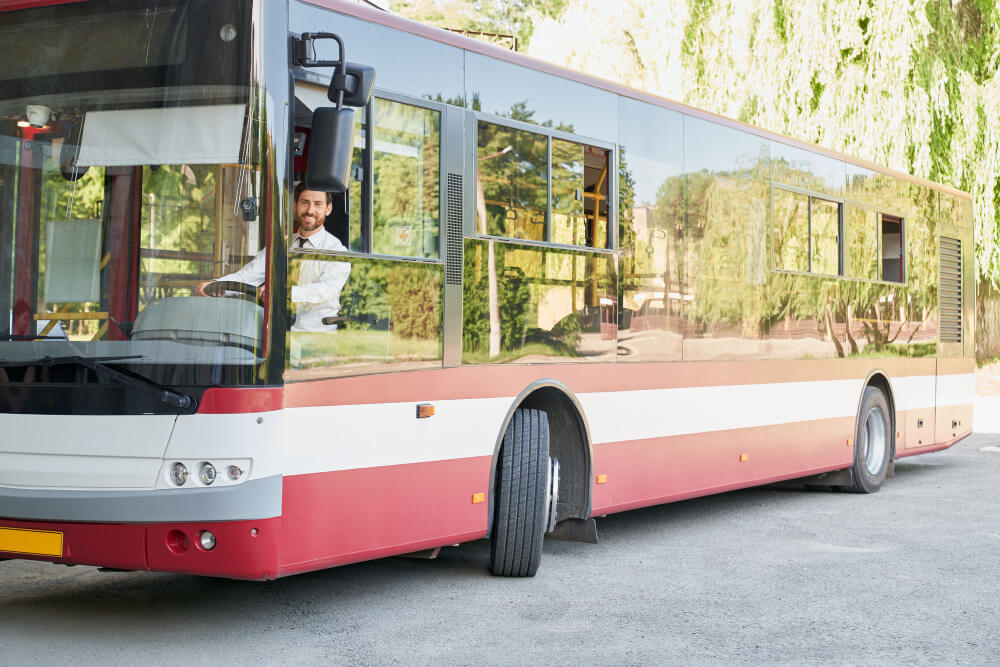 Ein Stadtbus des Stuttgarter Messe-Shuttles steht am Straßenrand, der Fahrer im weißen Hemd schaut heraus, Bäume spiegeln sich in den Scheiben